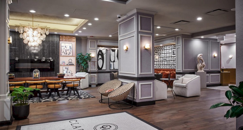 The image shows a stylish modern lobby with elegant furniture, artwork on the walls, a chandelier, and indoor plants.