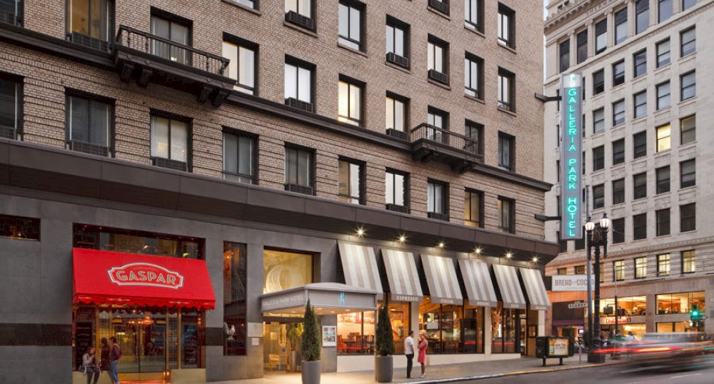 The image shows an urban street with buildings, including a hotel with a neon sign and a storefront with red and white awnings.