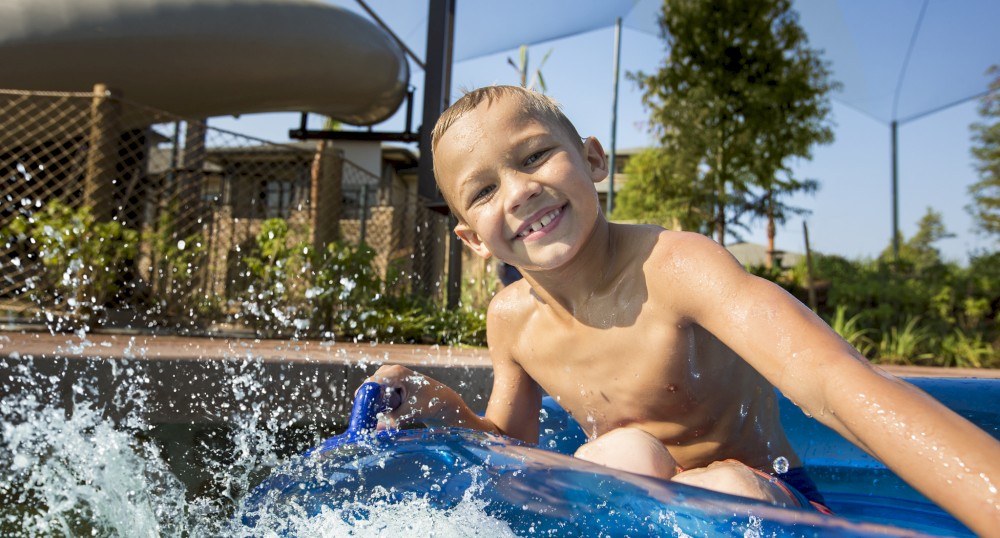 A young child is playing in a blue inflatable pool, smiling and splashing water. There