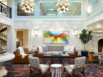 A modern living room features a large sofa, colorful artwork, a fireplace, chic lighting, and two armchairs around a small table.