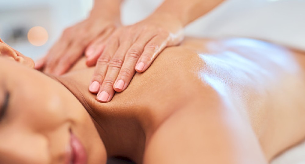 A person is receiving a back massage from another person, with focus on the shoulders and upper back, in a relaxed setting.