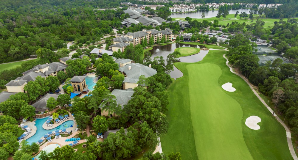 The image shows an aerial view of a resort with a large building complex, a swimming pool, and an adjacent golf course surrounded by dense greenery.