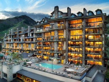 This image depicts a luxurious multi-story hotel with numerous balconies, an outdoor pool, and a mountain in the background at dusk.