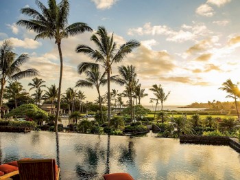The image captures a tropical paradise with palm trees, a tranquil pool, and a breathtaking sunset over a lush, green landscape.